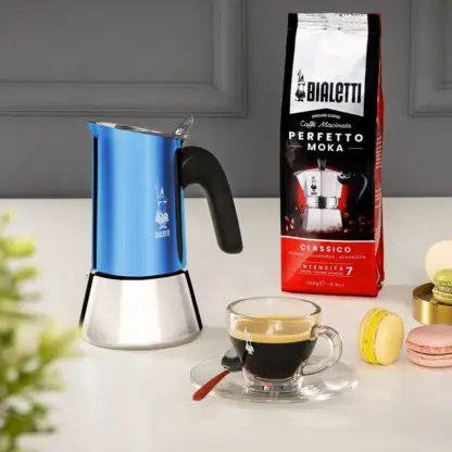 Bialetti Venus Blue Moka Pot paired with a cup off coffee, macaroons and a bag of ground coffee.