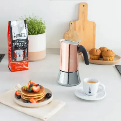 Bialetti Venus Copper Moka Pot on couter with cup of espresso, waffels and bag of perfetto koga ground coffee