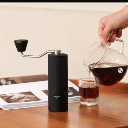 Chestnut C2S Portable Manual Coffee Grinder with a coffee being poured and a book in the background