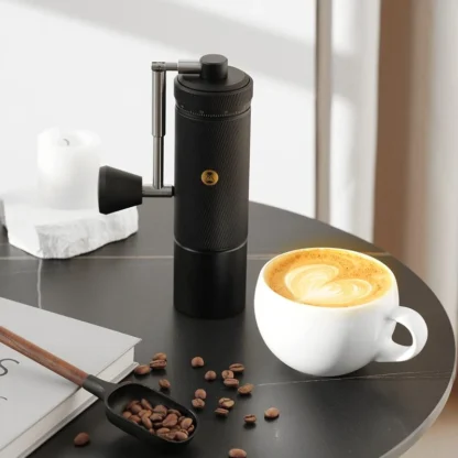 Chestnut S3 Portable Manual Coffee Grinder on table with a cappuccino in the foreground