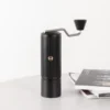 Chestnut X-lite Manual Portable Coffee Grinder on a table next to a stack of books